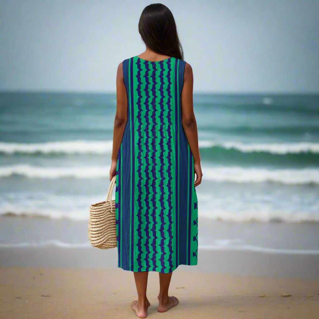 Woman in a blue and green kuffiyeh dress standing on a beach