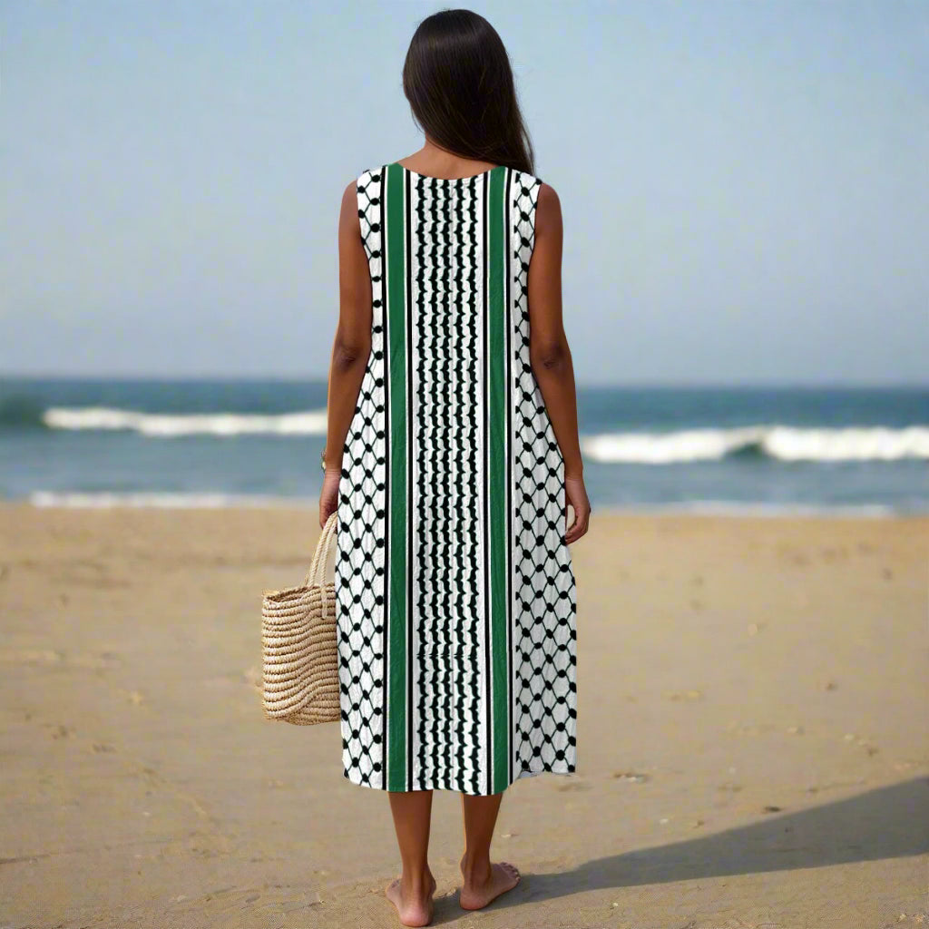 Woman in a sleeveless kuffiyeh dress with green and black pattern standing on a beach.