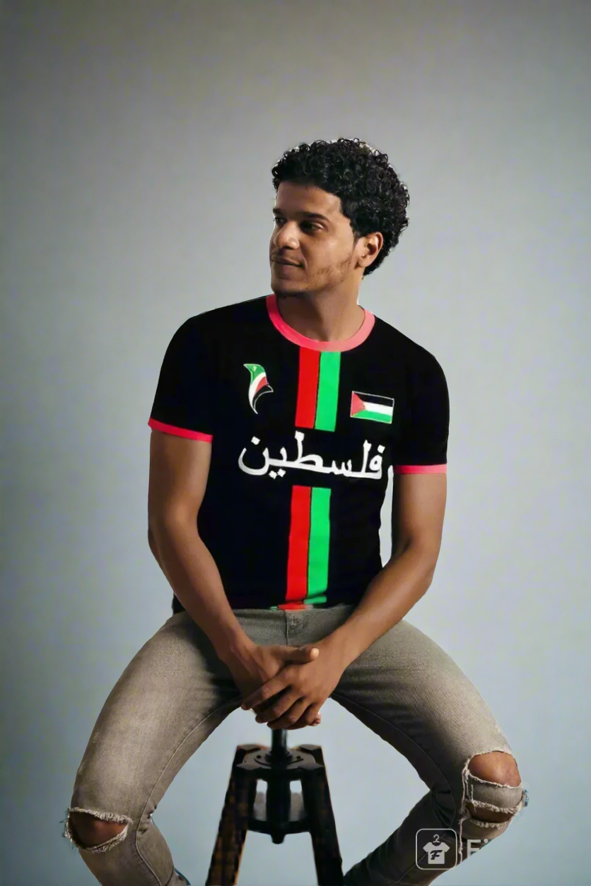 Person wearing a black Palestine Jersey t-shirt with red and green stripes and Arabic text, sitting on a stool against a white background.