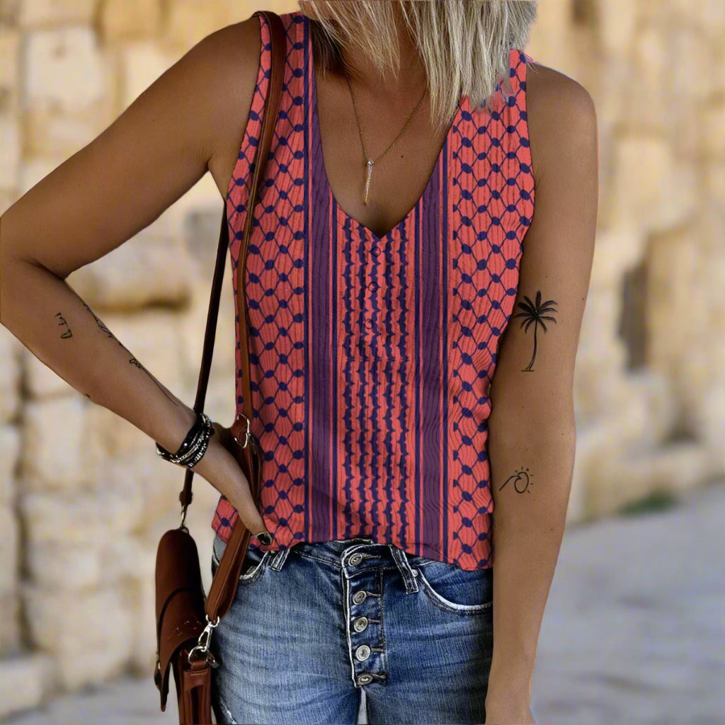 Person wearing a patterned sleeveless keffiyeh top and jeans against a gray wall.
