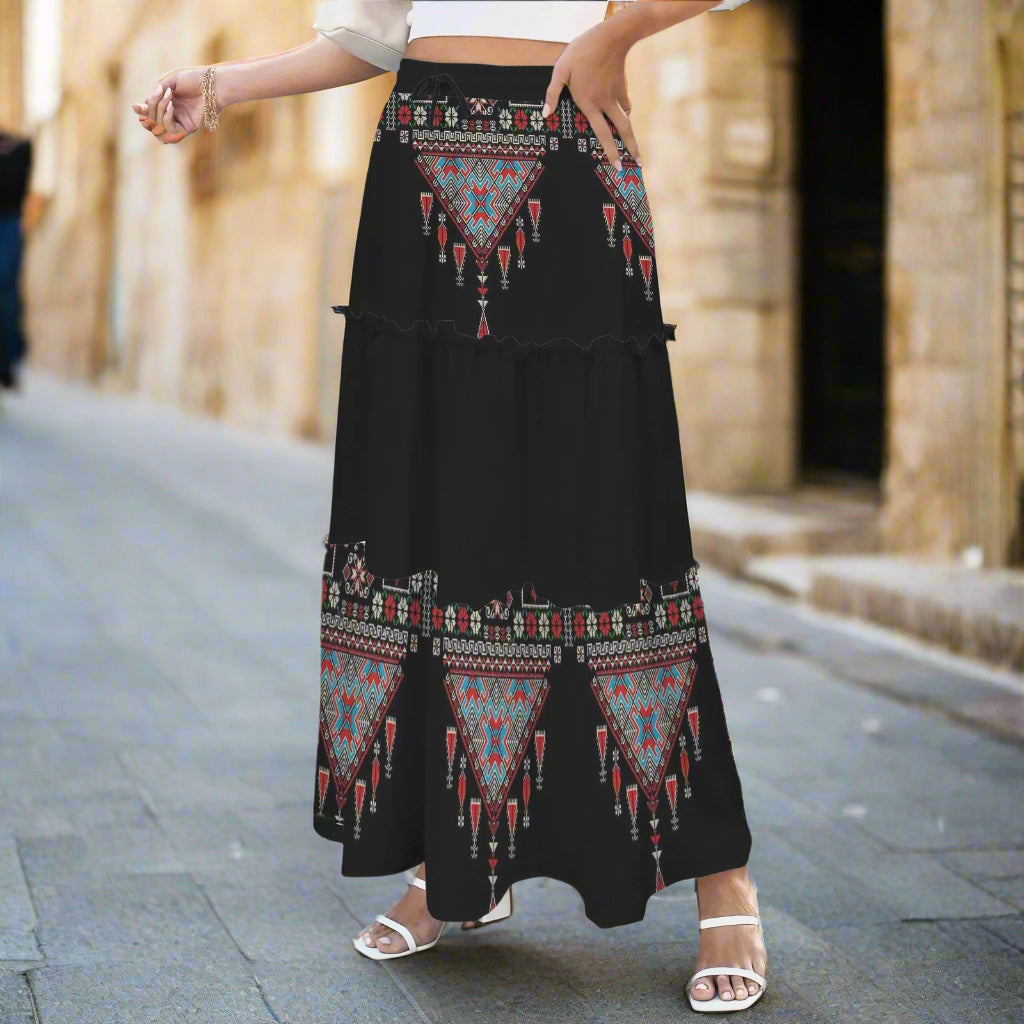 Person wearing a black tatreez palestinian skirt with geometric patterns outdoors.