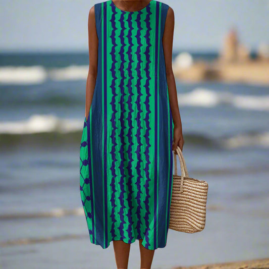 Person wearing a green and blue kuffiyeh patterned dress on a beach