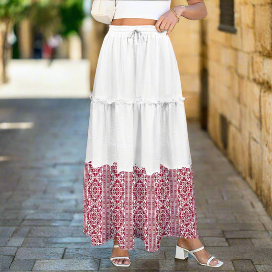 Woman wearing a white skirt with red tatreez patterned hem in an outdoor setting.