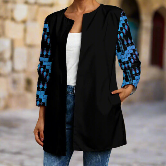 Person wearing a black cardigan with blue geometric patterns representing tatreez from palestinian, standing against a stone wall in jerusalem.