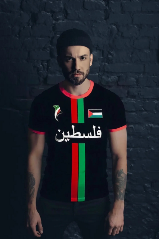 Person wearing a black t-shirt with red and green stripes and Arabic text  palestine against a dark brick wall.