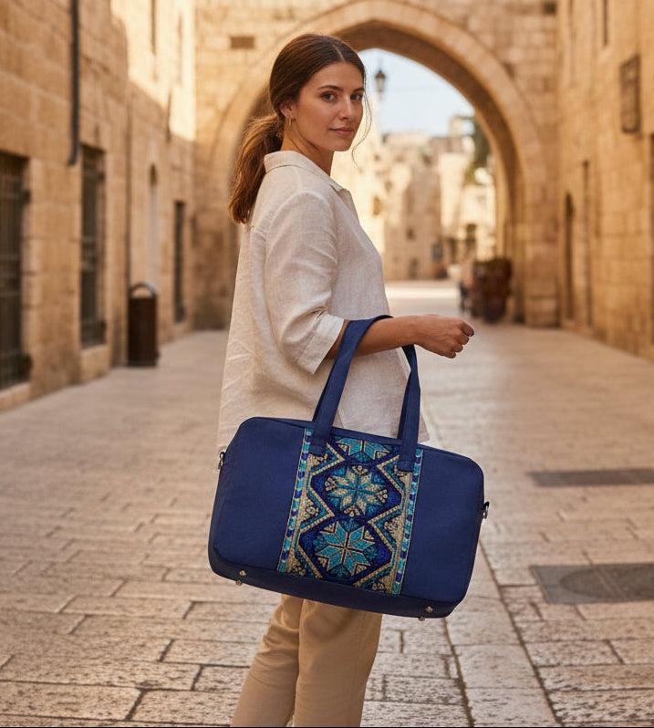 Woman holding a blue tatreez bag with intricate patterns in an old stone street.