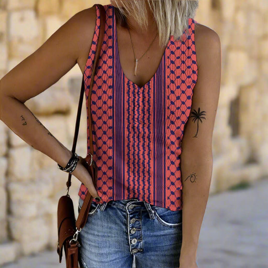 Person wearing a patterned sleeveless keffiyeh top and jeans against a gray wall.