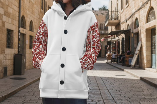 Person wearing a white hoodie with red tatreez patterned sleeves on a street.