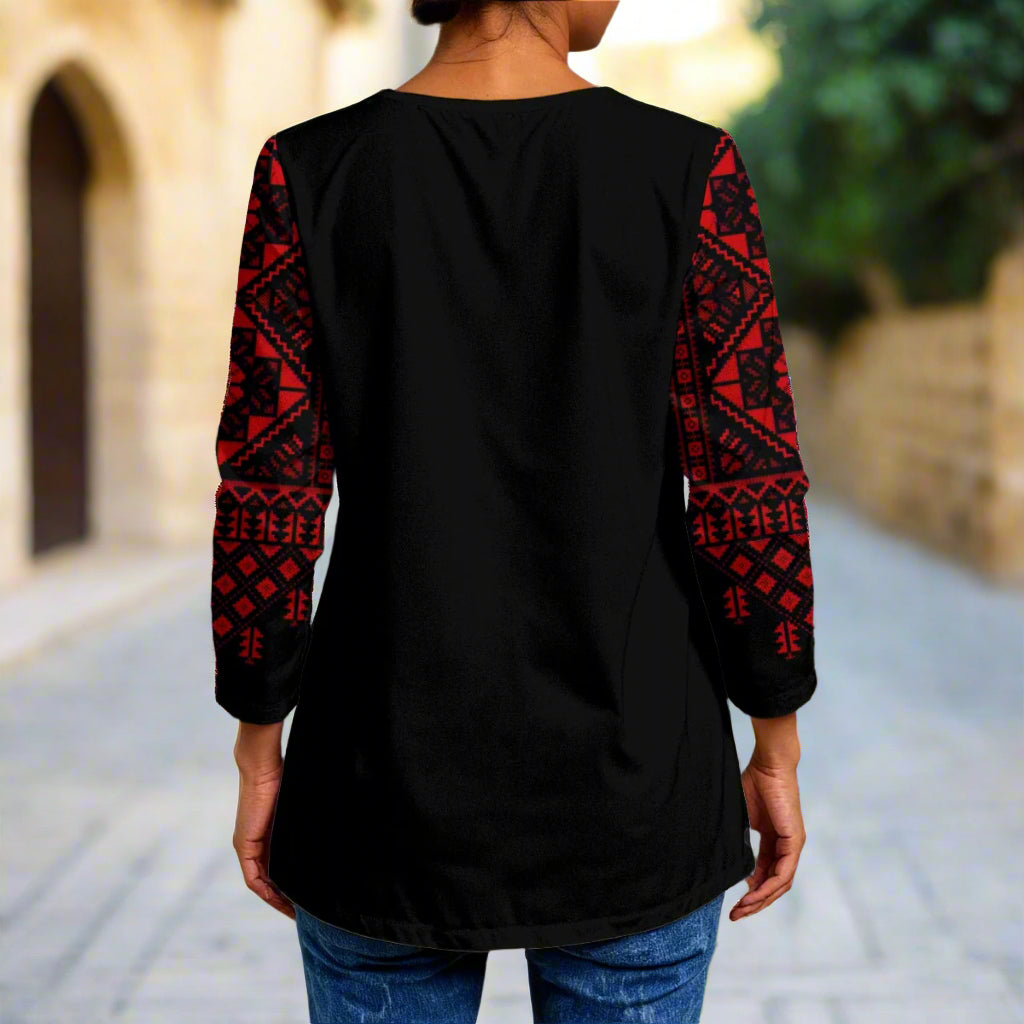 Person wearing a black top with red patterned sleeves standing in front of a textured wall.
