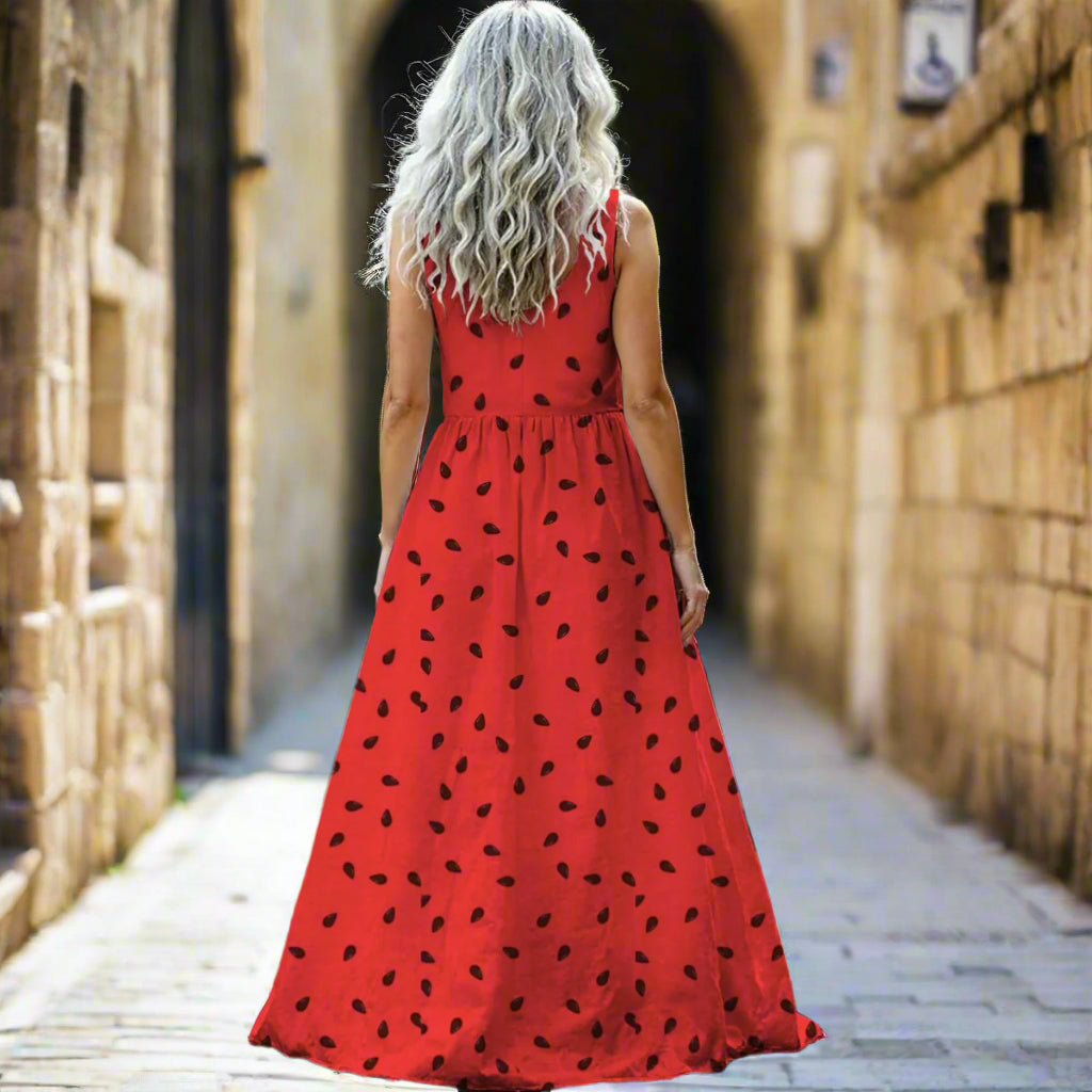 Woman in a red dress with watermelon with black patterns walking outdoors.