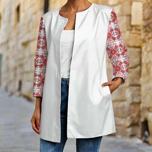 Person wearing a white cardigan with red floral sleeves of tatreez print palestinian patternagainst a stone wall.